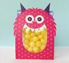 Pink monster-shaped party favor box with clear window filled with yellow candies