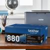 Brother TN880 high-yield toner cartridge in front of wireless laser printer on desk