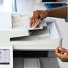 Hand retrieving color documents from Brother all-in-one laser printer scanner in office