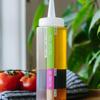 Squeeze bottle with olive oil, balsamic vinegar, and honey beside fresh tomatoes