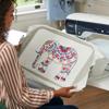 Woman using Brother embroidery machine with colorful elephant design in home workspace
