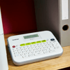 Brother P-touch label maker with LCD screen and QWERTY keyboard on wooden shelf