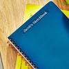 Etiqueta Brother TZe en cuaderno espiral azul con texto personalizado sobre escritorio de madera