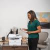 Woman reviewing printed document from Brother MFC-L2980DW monochrome laser all-in-one printer in home office