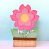 Pink paper flower craft with yellow center in decorative pot on white surface