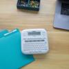 Brother PT-D220 label maker with QWERTY keyboard on desk beside teal folders and laptop