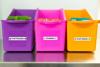 Purple, pink, and orange fabric storage bins labeled for fruit pouches, crackers, and snacks