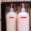 Two white pump bottles with red labels labeled Shampoo and Conditioner on wooden shelf