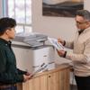 Two professionals reviewing color prints from Brother all-in-one printer in office setting