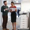 Two professionals reviewing documents beside Brother laser printer with multiple paper trays in office