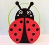 Red and black ladybug-shaped lunch bag with yellow handles on pink surface