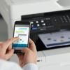 Person using smartphone to print wirelessly with Brother all-in-one color laser printer in office