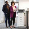 Two professionals reviewing documents beside Brother laser printer with paper trays in office