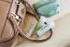 Travel-size labeled bottles with shampoo beside tan handbag and teal toiletry pouch