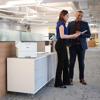 Brother HL-EX415DW wireless laser printer on office desk with professionals collaborating