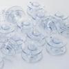 Clear plastic sewing machine bobbins arranged on white surface