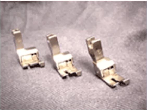 Three metal presser feet for Brother sewing machines on gray fabric background