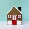 Cardboard gingerbread house craft with red door, white fence, and snow-covered roof