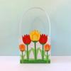 Decorative paper gift bag with colorful tulip flowers and clear handle on white surface