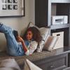 Child using tablet on couch with Brother MFC-J1205W wireless all-in-one printer on shelf