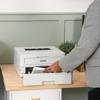 Person loading paper into Brother HL-L2865DW wireless monochrome laser printer on desk