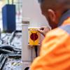 Worker in safety vest applying Brother label to industrial electrical panel outdoors