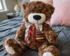 Brown plush teddy bear with white paws and red ribbon sitting on gray bedding