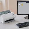 Brother ADS-4300N desktop document scanner on office desk with computer monitor displaying scan options