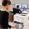 Woman loading paper into Brother HL-L6415DWT monochrome laser printer in office workspace