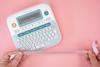 Hands holding decorative ribbon next to Brother P-touch label maker on pink surface