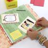 Hands placing photo and invitation in scrapbook with colorful patterned paper and stickers