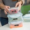 Person organizing labeled food storage containers with fresh chillies, parsley, and peppers