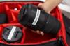 Hand placing camera lens in padded red organizer bag with protective compartments