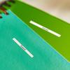 Cinta de etiquetas no laminada Brother en cuadernos turquesa y verde con espiral