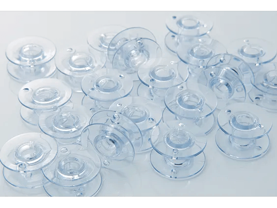 Clear plastic bobbins for Brother sewing machines arranged on white surface