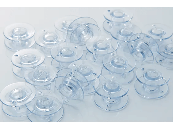 Clear plastic bobbins for Brother sewing machines arranged on white surface