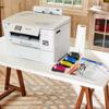 Brother PrintModa wireless color printer on table with ink cartridges and fabric roll