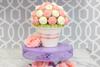 Cupcake bouquet with pink and white frosting arranged in white pot on purple stand