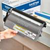 Hand holding Brother TN-750 black toner cartridge with packaging in background