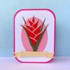 Paper craft tropical flower with red petals and green leaves in pink frame
