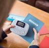 Brother PT-M95 handheld label maker printing name tag on blue folder