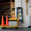 Yellow utility cart with safety cones, ladder, and cleaning tools in storage area