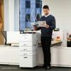 Man reviewing documents beside Brother laser printer with paper tray tower in modern office