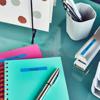 Brother label maker on desk with turquoise notebook, pink sticky notes, and pens