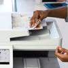 Person retrieving color documents from Brother all-in-one printer scanner in office workspace