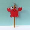 Red crab pencil topper with googly eyes on yellow pencil against blue background